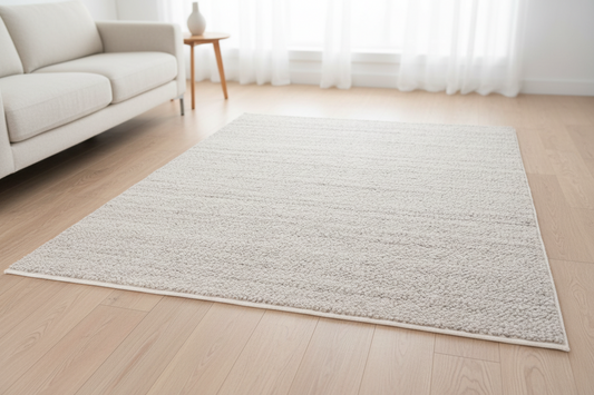 Beige rug on a wooden floor in a living room with a sofa and side table.