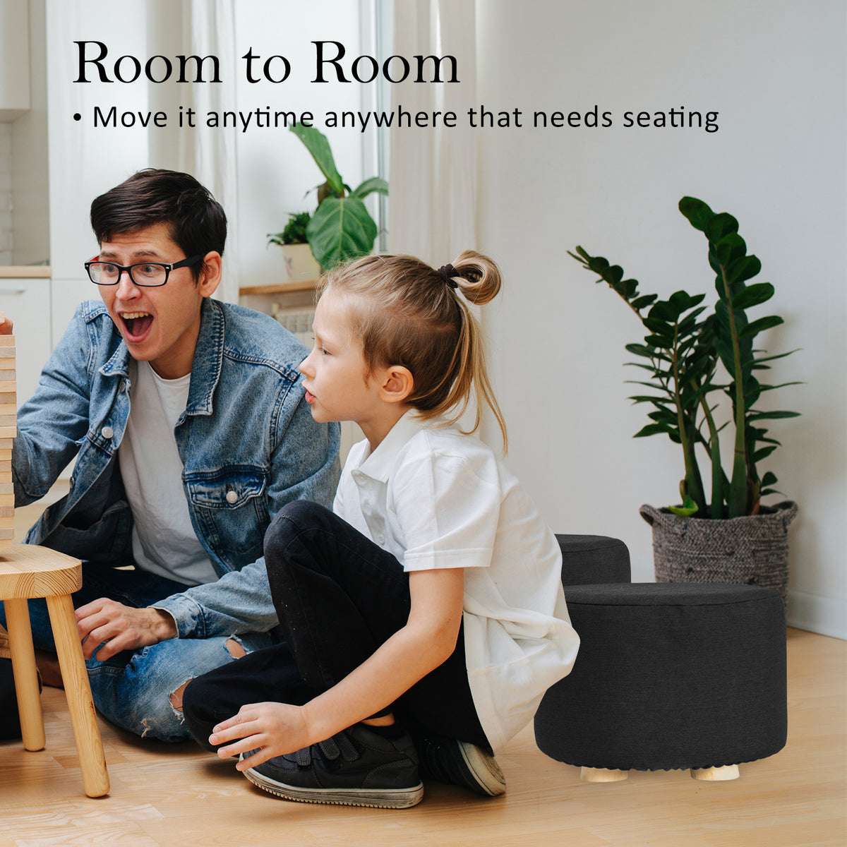 Man and child sitting on the floor with a black ottoman in a room setting.