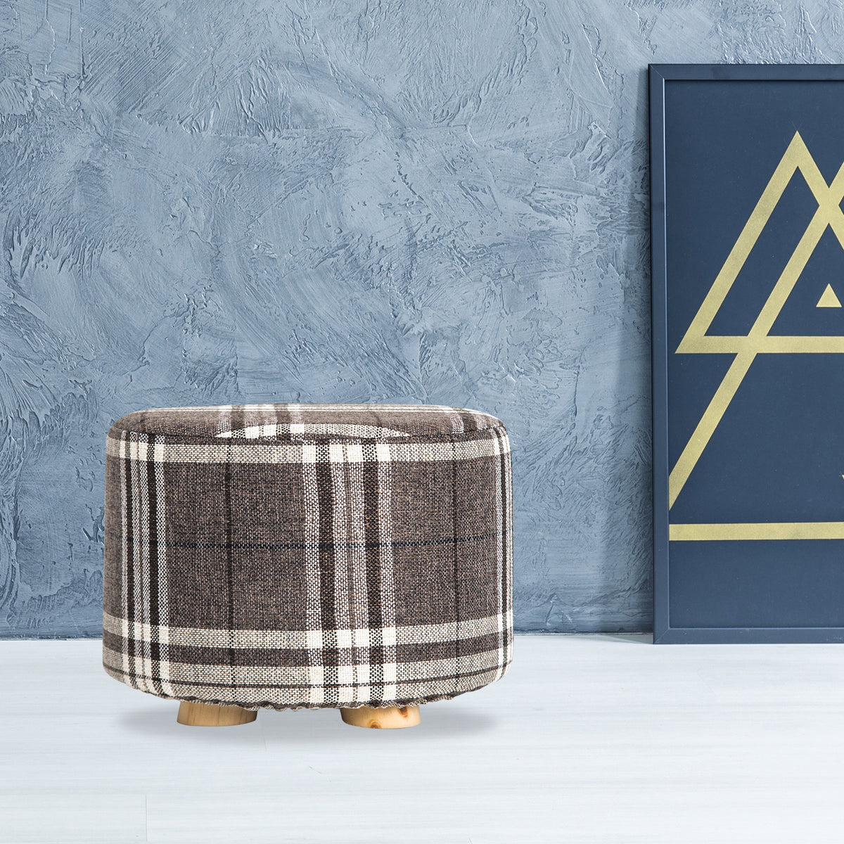 Plaid ottoman against a textured gray wall with a geometric art piece.