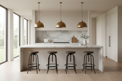 A modern kitchen island with a white marble countertop and backsplash, four black metal bar stools with brown wooden seats, three bronze dome pendant lights, and large windows on the left.