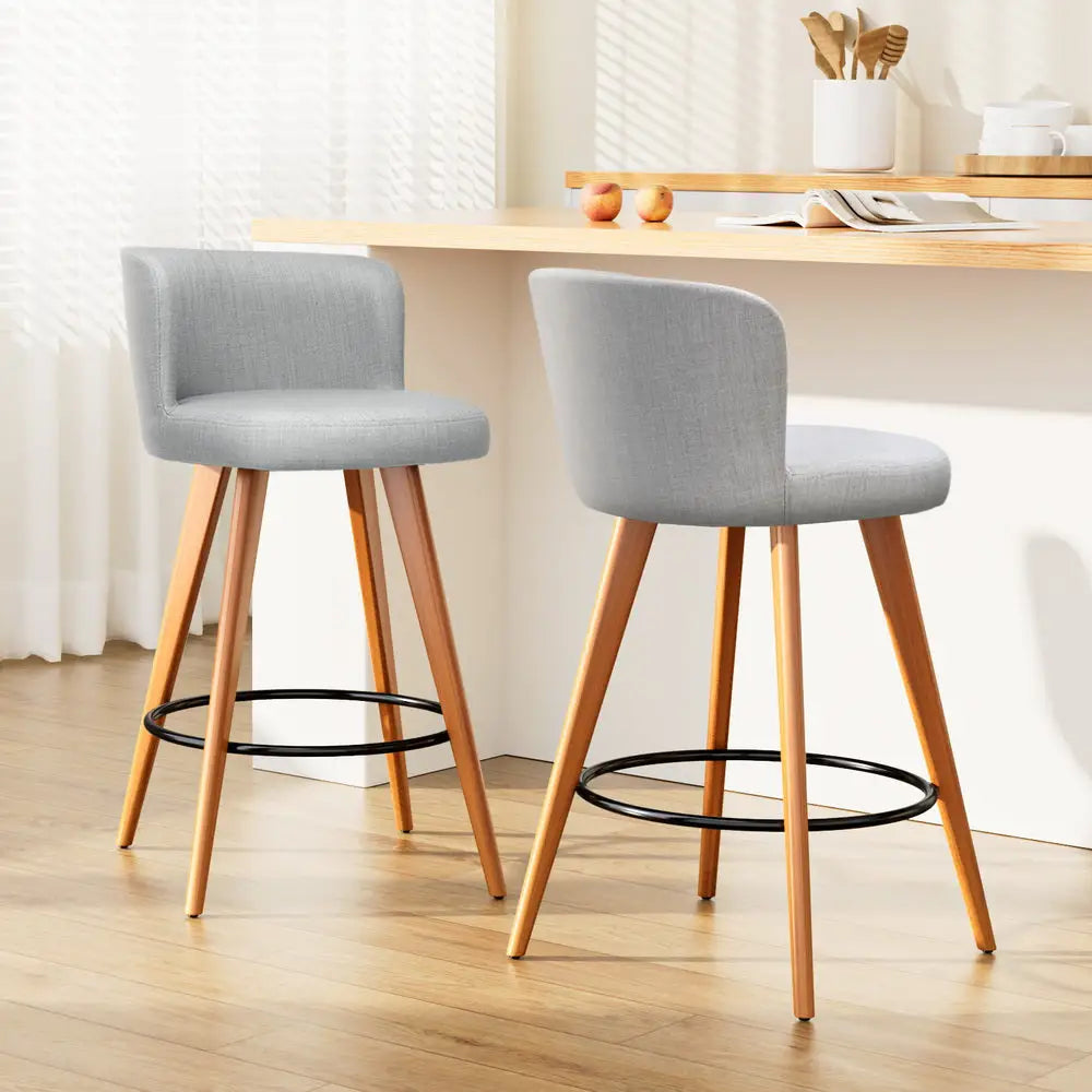 2 grey seat bar stools with wooden legs, padded seats with back rest and including round leg rest all around in modern kitchen with white walls and white cabinets
