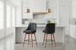 2 charcoal seat bar stools with wooden legs, padded seats, swivel seats and including leg rest all around in modern kitchen with white walls and white cabinets