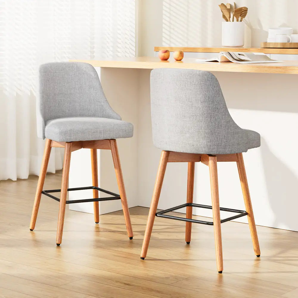 2 grey seat bar stools with wooden legs, padded seats, swivel seats and including leg rest all around in modern kitchen with white walls and white cabinets