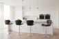 A modern kitchen island with a white marble countertop and backsplash, surrounded by four bar stools in a bright, contemporary kitchen with white cabinetry and double built-in ovens.