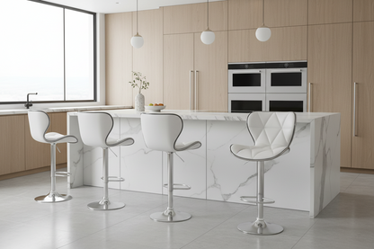 A modern kitchen island with a white marble-look countertop and matching base, surrounded by four white bar stools with silver metal bases. The background features light wood cabinets, built-in stainless steel ovens, and white globe pendant lights.
