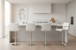 A modern kitchen island with four white bar stools featuring chrome bases, set in a bright, minimalist kitchen with light wood floors and white cabinetry.
