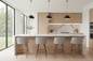 A modern kitchen island with a white marble-look countertop, light wood cabinetry, three black pendant lights, and four gray upholstered bar stools with wooden legs, set in a bright contemporary kitchen with large windows.