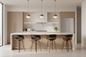 A modern kitchen island setup with a white marble countertop and backsplash, light wood cabinetry, three pendant lights, a stainless steel refrigerator, and four bar stools with black seats and brown wooden legs.