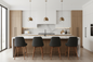A modern kitchen island setup with four dark gray upholstered bar stools featuring wooden legs, set against a kitchen backdrop with light wood cabinets, a white marble backsplash, and three bronze dome pendant lights.