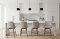 A modern kitchen island with four light gray upholstered bar stools featuring wooden legs, set against white cabinetry and a marble backsplash.