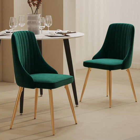Two green velvet chairs with gold legs in a dining setting.