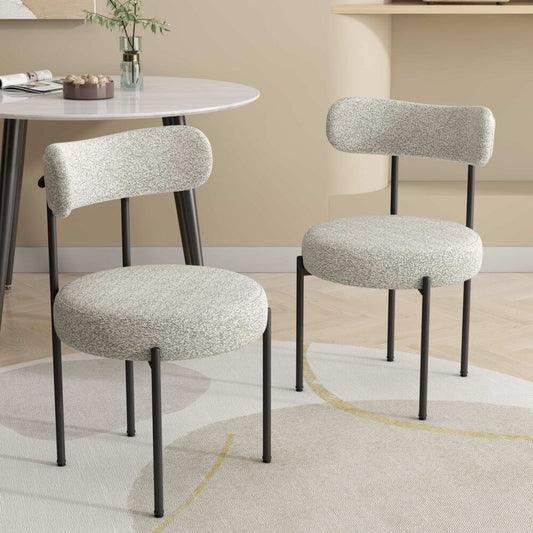 Two gray cushioned chairs with black legs in a room with a table and decor.