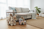 Two round wire baskets with wood-look tops are styled in a bright living room next to a light gray sofa, filled with plush toys and blankets.
