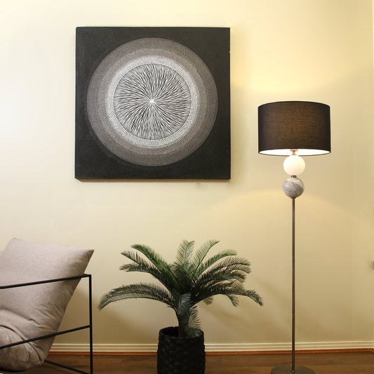 Modern interior with a circular artwork, floor lamp, and potted plant on a neutral wall.