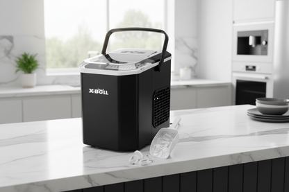 A black X-Bull portable ice maker with a clear lid and handle sits on a white marble kitchen countertop, with ice cubes and a clear scoop in front of it.